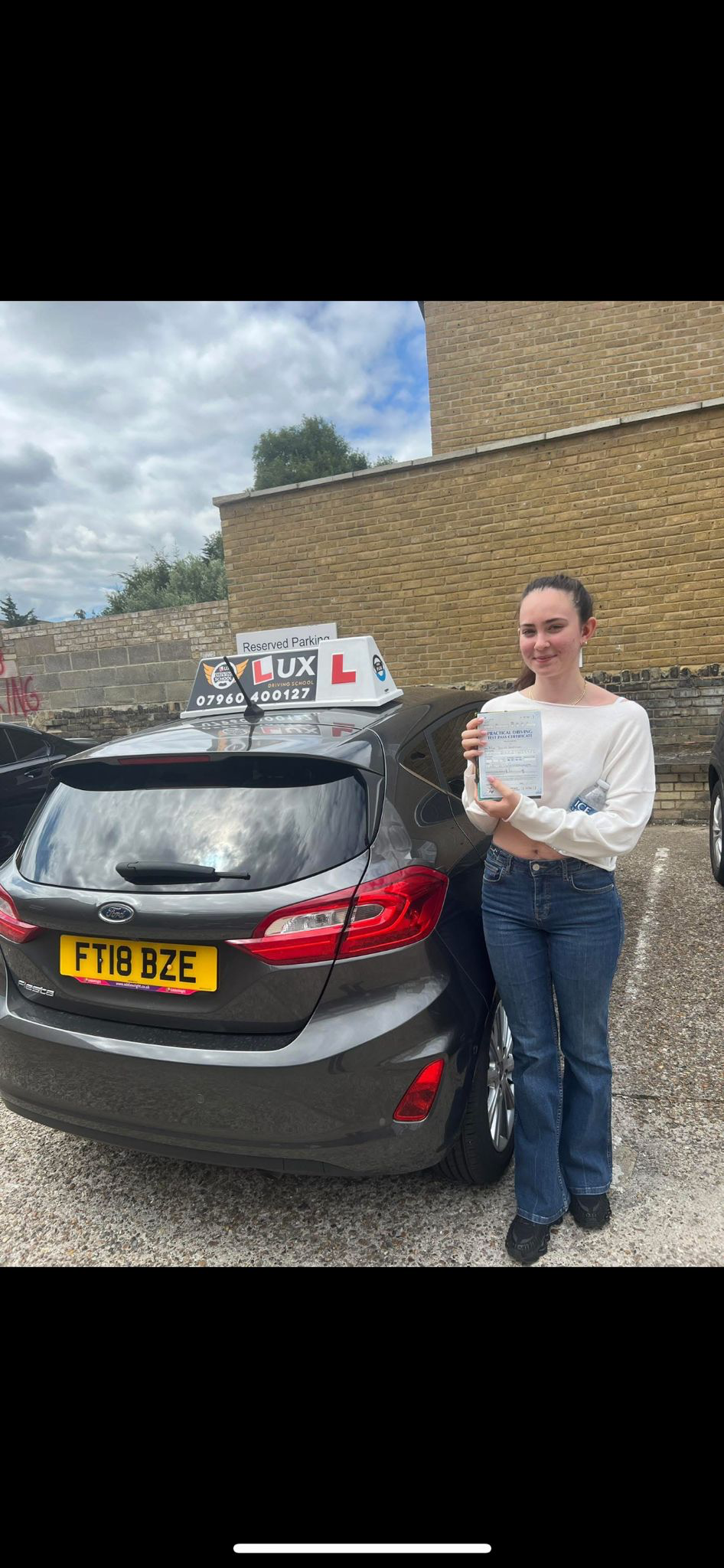 Successful female student with pass certificate next to Lux Driving School car