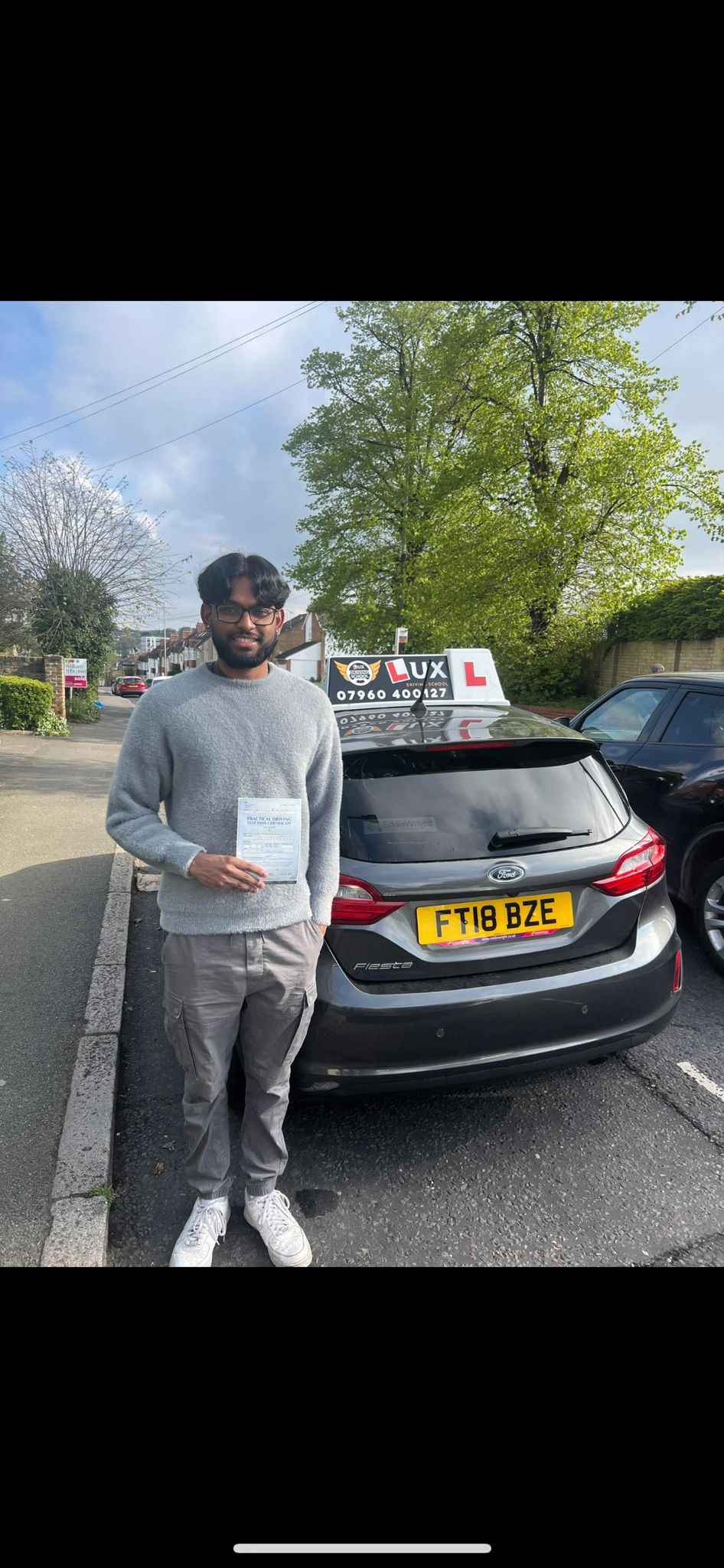 Successful male student with pass certificate next to Lux Driving School car