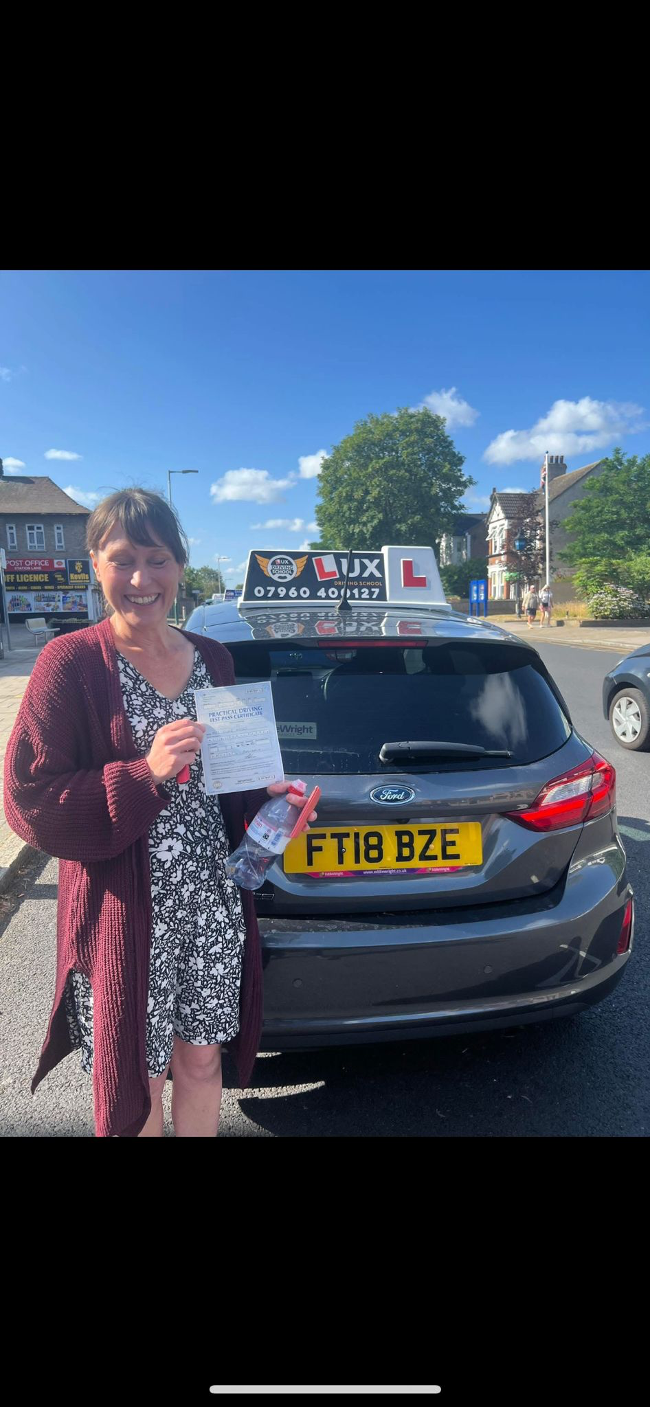 Successful female student with pass certificate next to Lux Driving School car